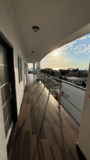 A corridor with a tiled floor leading to a balcony with a glass railing. - CUATRO PALMAS HOTEL  (Puerto Peñasco)