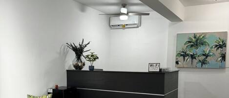 A reception area with a black reception desk, a beige armchair, a potted plant, and a painting of palm trees on the wall.