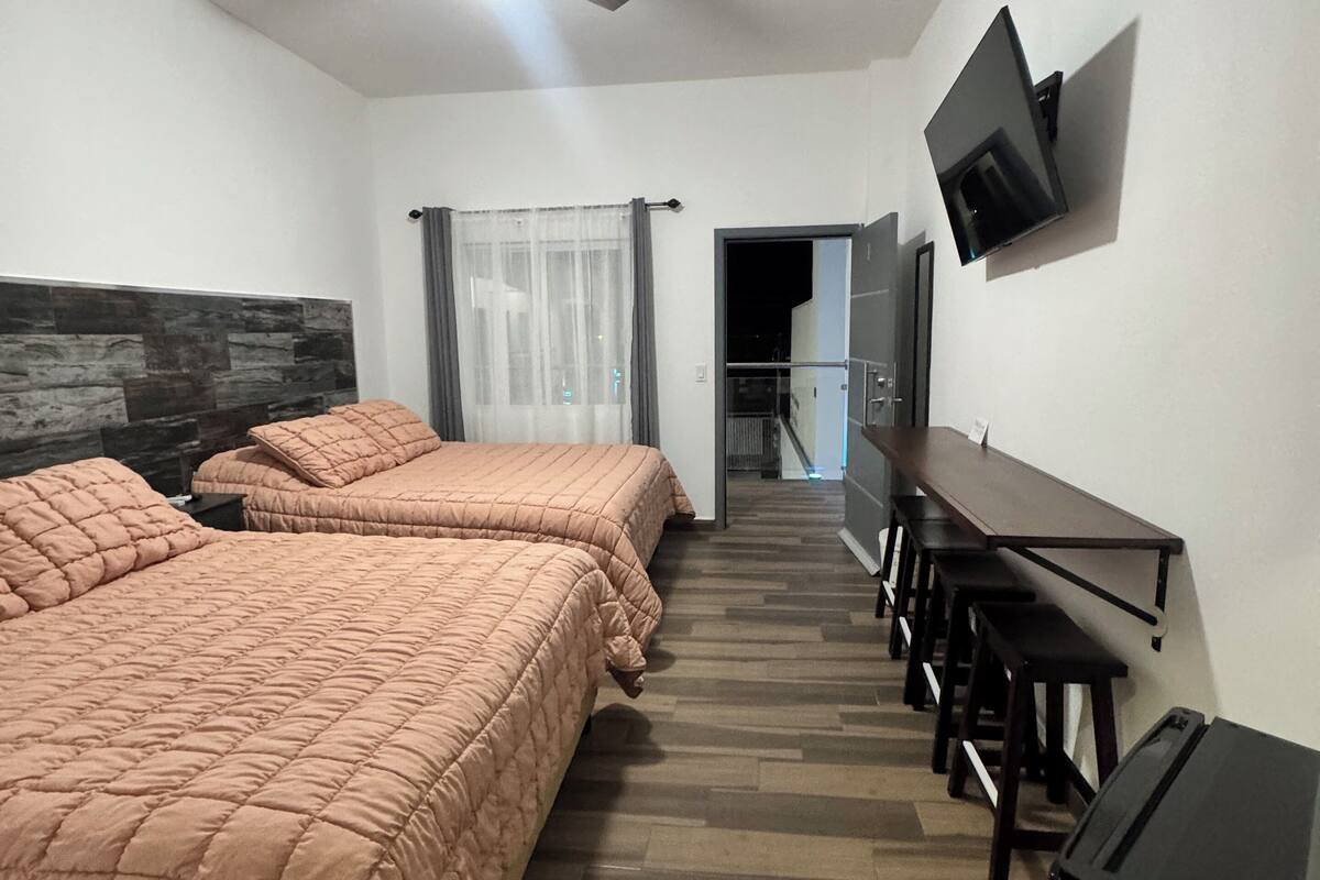 A hotel room with two beds, a ceiling fan, a TV mounted on the wall, and a desk with chairs.