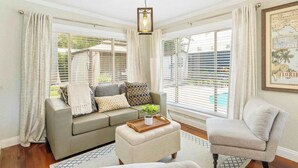 A living room with a sofa, ottoman, and armchair, a hanging light fixture, and a framed map on the wall. - 2 miles to Beach~ Pool ~Cabana~ Pool Table (Deerfield Beach)