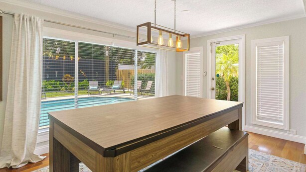 A poolside room with a wooden table, a hanging light fixture, and large windows with blinds. - 2 miles to Beach~ Pool ~Cabana~ Pool Table (Deerfield Beach)