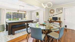 A dining area with a glass table, blue chairs, a wooden bench, and a television on a wooden stand. - 2 miles to Beach~ Pool ~Cabana~ Pool Table (Deerfield Beach)