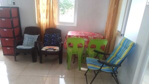 Una habitación con piso de baldosas, una mesa cubierta con mantel rojo, y cuatro sillas de diferentes diseños y colores.