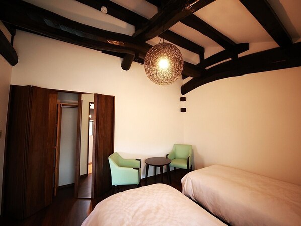 Una habitación con dos camas, una mesita, dos sillas y una lámpara colgante.