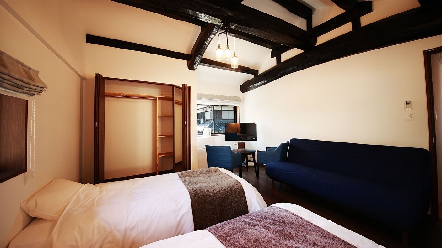 A hotel room with two beds, a blue sofa, a TV, and a wooden wardrobe.