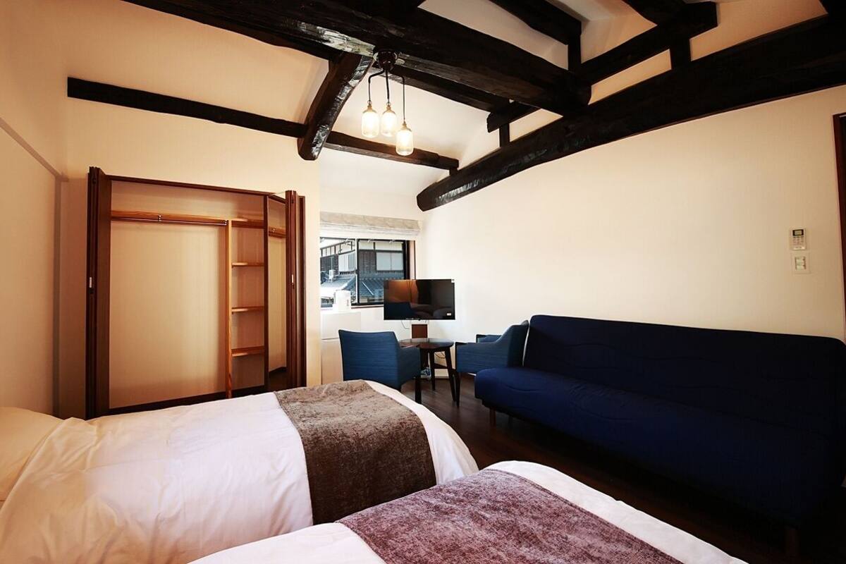 Una habitación de hotel con dos camas, un sofá azul, un televisor y un armario de madera.