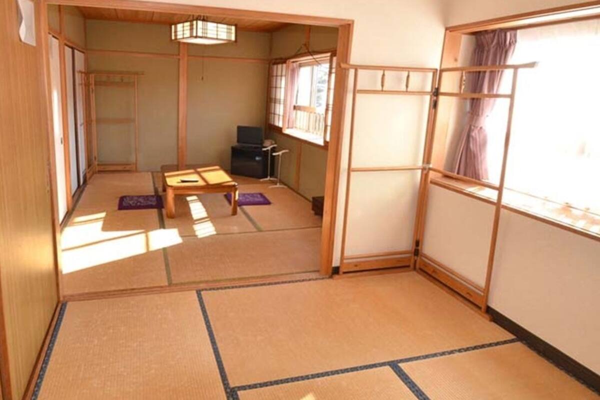 Una habitación japonesa tradicional con suelo de tatami, una mesa baja, un televisor y puertas correderas.