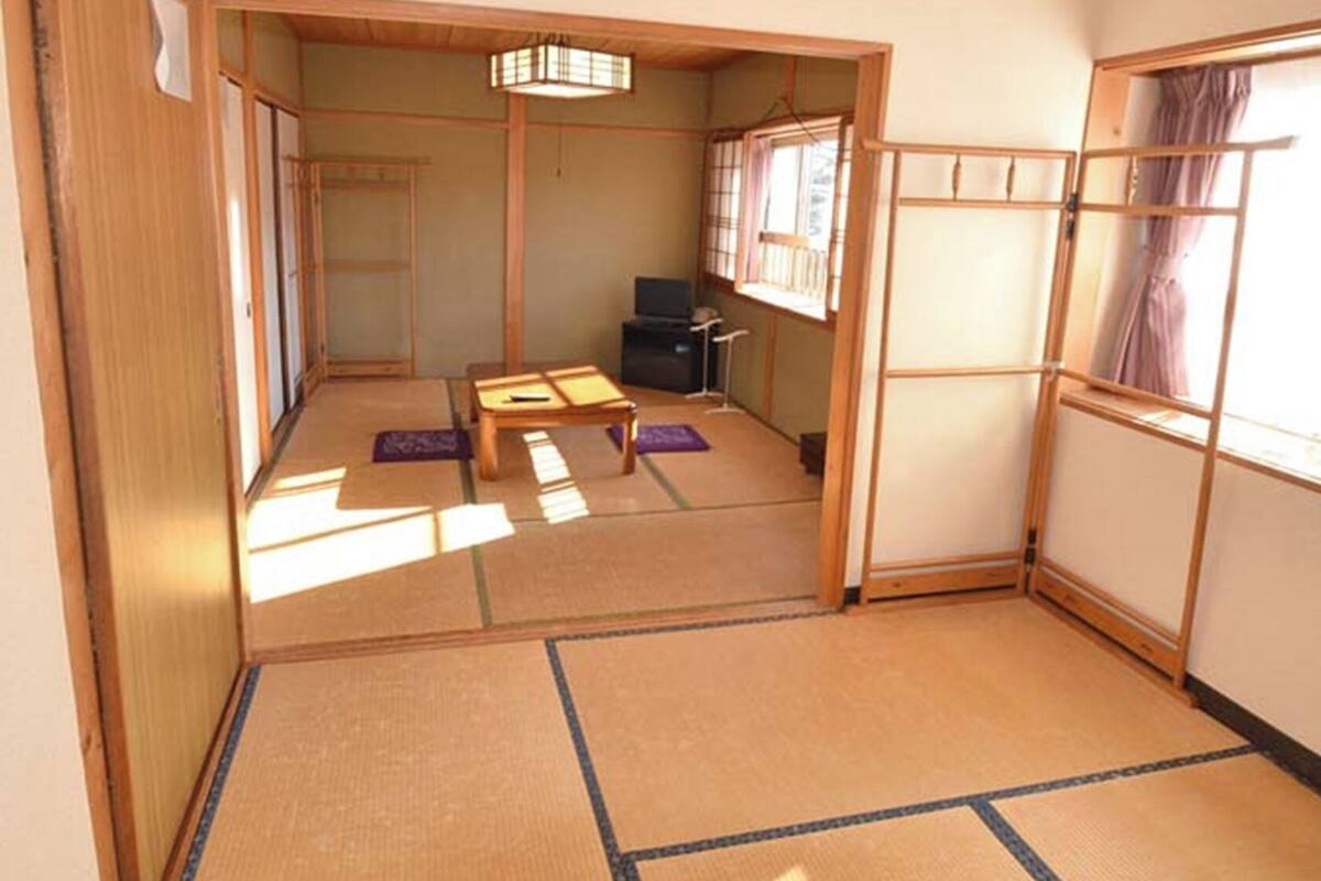 A traditional Japanese room with tatami flooring, a low table, cushions, and sliding doors.