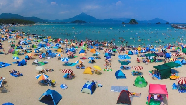 A crowded beach with numerous colorful umbrellas and tents. - Kaemon Ryokan (Takahama)