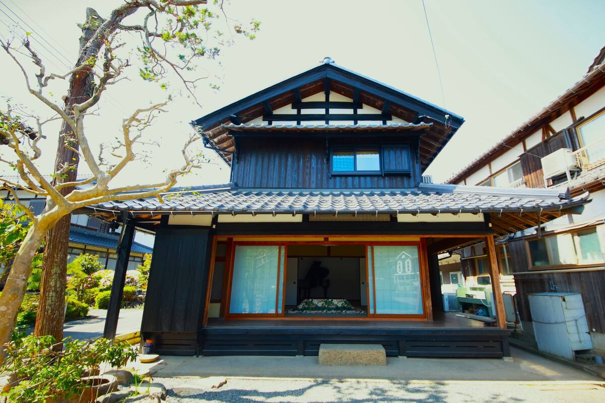 A traditional Japanese house with a tiled roof, wooden structure, and a small porch.