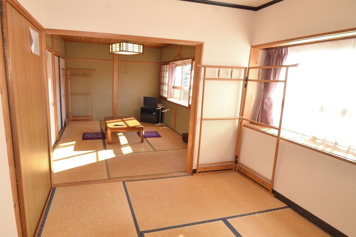 A traditional Japanese room with tatami flooring, a low table, a TV, and a sliding door leading to another room.