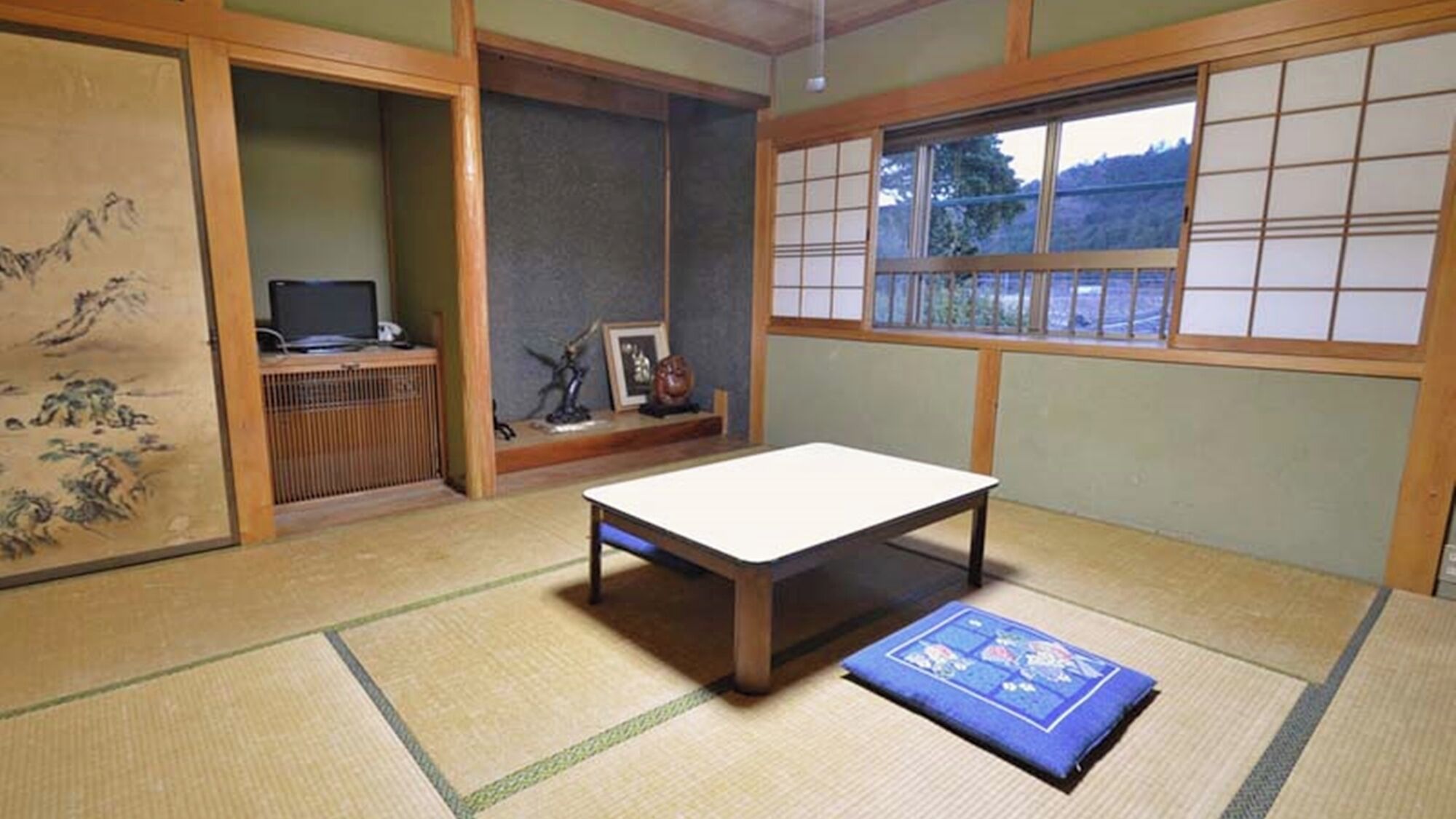 Et rum med tatamimåtter, et lavt bord, en tatamipude, en shoji-skærm og et traditionelt japansk maleri.