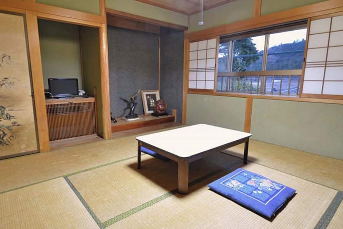 A tatami mat room with a low table, a tatami mat cushion, a shoji screen, and a traditional Japanese painting.