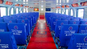 A row of blue seats with red carpeting and a television screen at the end of the aisle. - Aman Dia Cruise (Serangan)