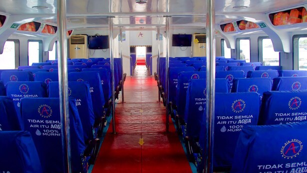A bus interior with blue seats, a red floor, and a central aisle. - Aman Dia Cruise (Serangan)