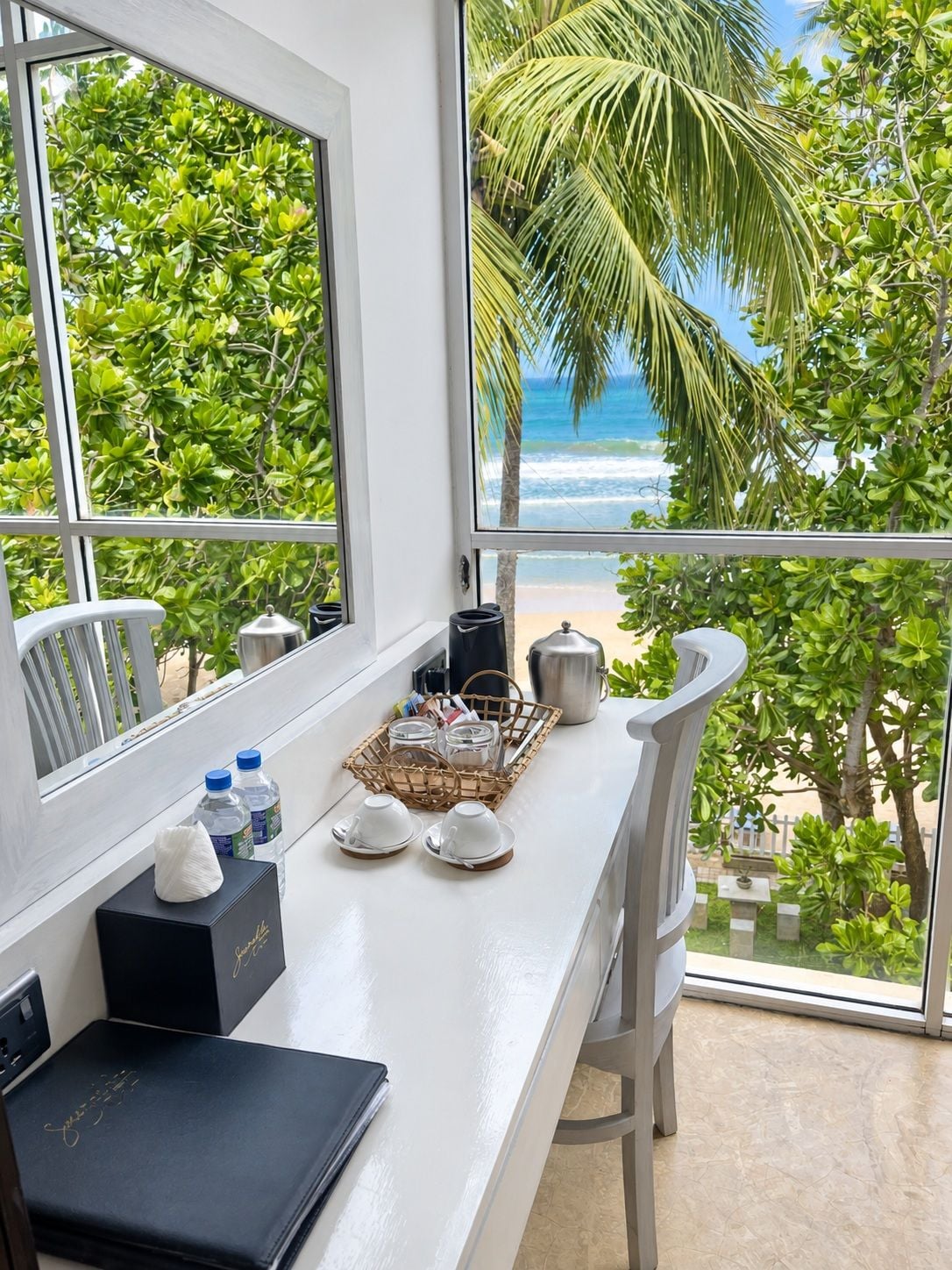 A balcony with a view of the ocean, a coffee pot, a basket with cups, and a black box with gold lettering.