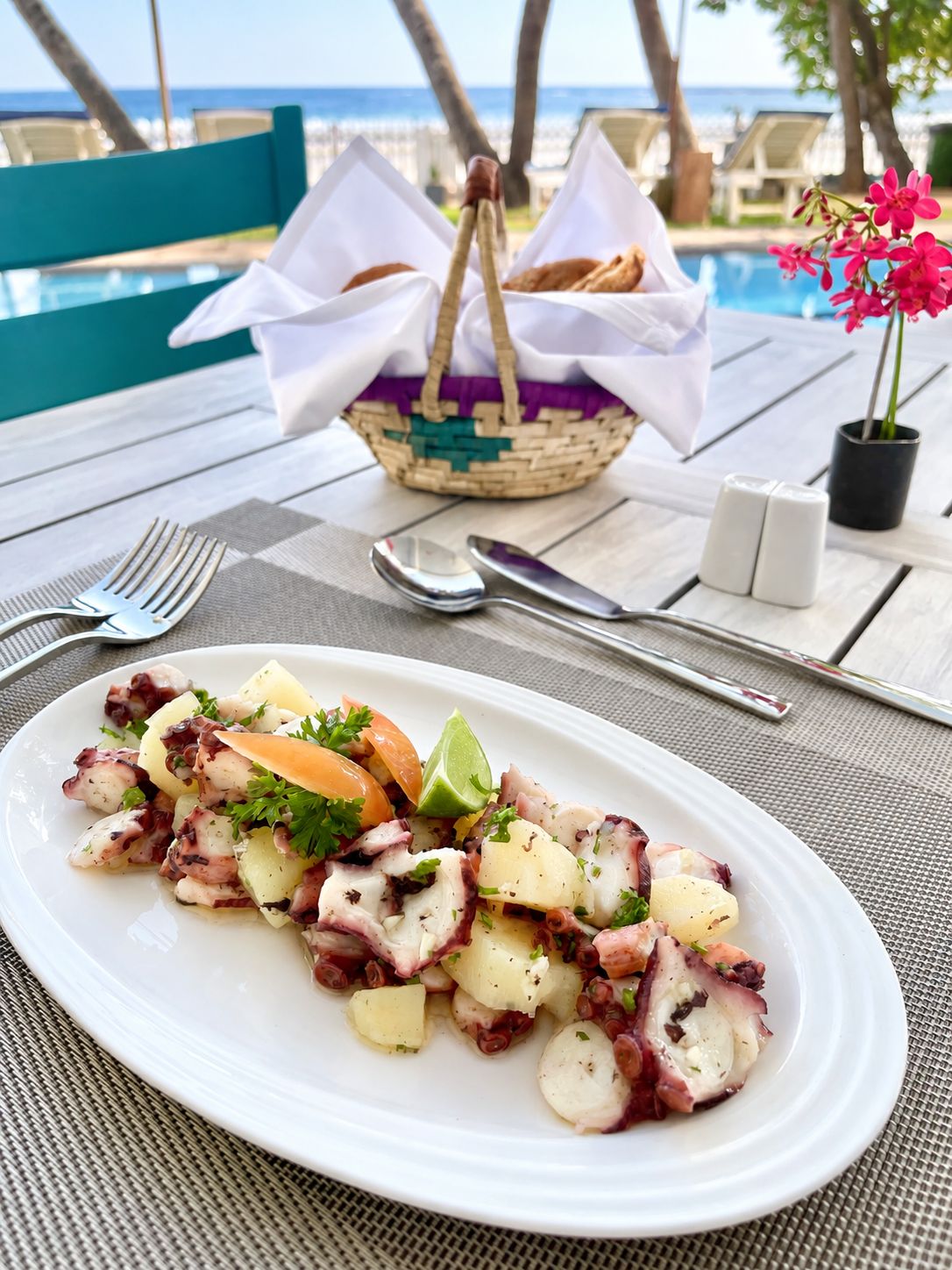 A table set with a plate of octopus salad, a basket, and a view of the ocean.