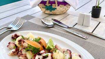 Una mesa dispuesta con una ensalada de pulpo, una cesta y vistas al océano.
