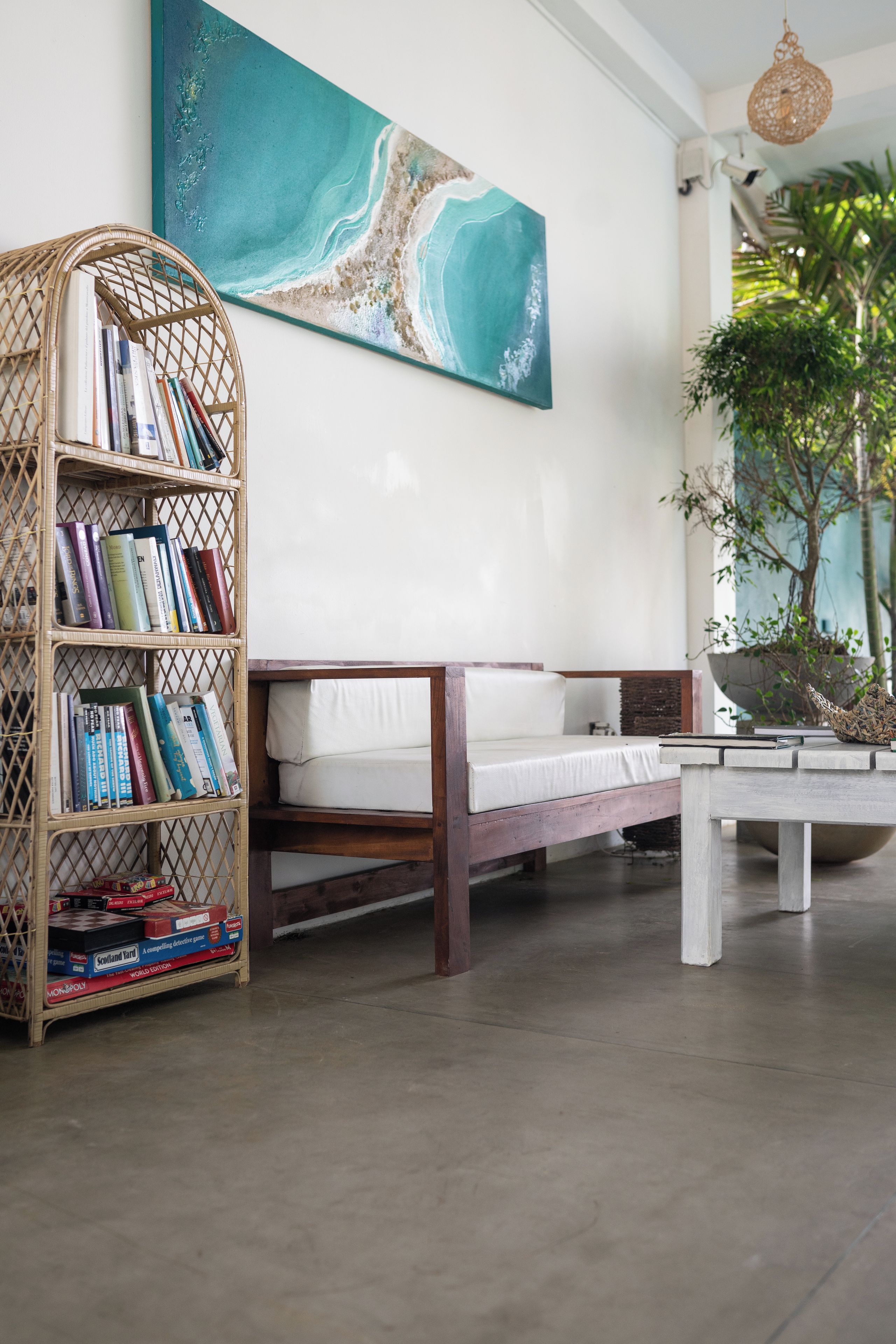 A room with a wooden bookshelf, a white sofa, and a painting of a beach scene.