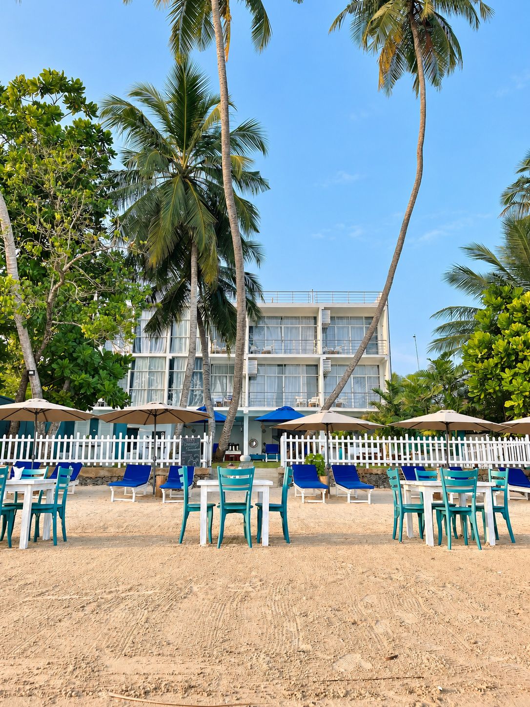 A beachfront hotel with outdoor seating and palm trees.