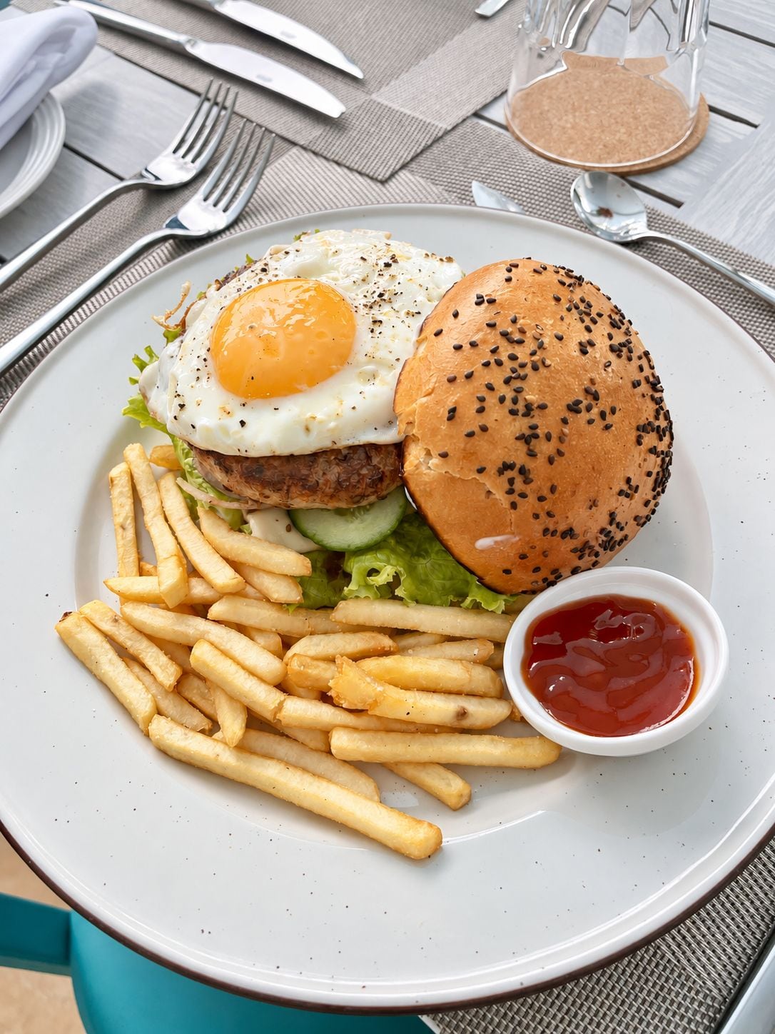 A plate with a burger, egg, fries, and ketchup.