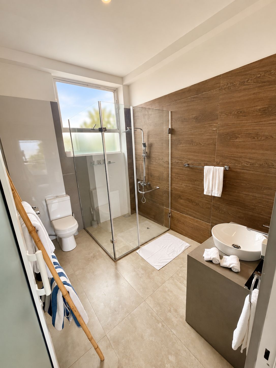 A modern bathroom with a glass-enclosed shower, a toilet, a sink, and a large window.