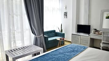 Una camera d'albergo moderna con un letto, una scrivania, una televisione e un tavolino con una pianta.