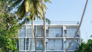 Ein Hotel direkt am Strand mit mehreren Etagen, Palmen und blauen Liegestühlen mit Sonnenschirmen.