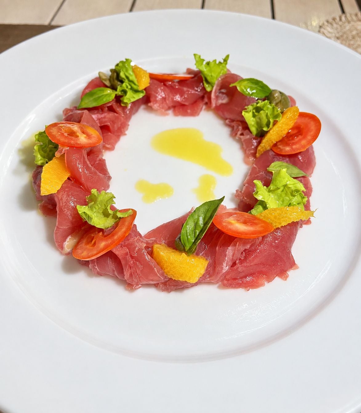 Un piatto bianco con un'ordinata disposizione di fettine sottili di carne, guarnito con lattuga e fette di pomodoro, e un cucchiaio di salsa gialla al centro.