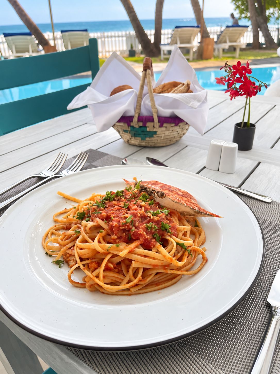 A dining table with a plate of spaghetti, a basket of bread, and a small potted plant.