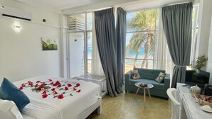 Ein Hotelzimmer mit Bett, Schreibtisch, Stuhl, kleinem Tisch und Blick auf den Strand.