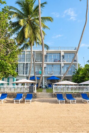 A beachfront hotel with a two-story structure, multiple balconies, and a sandy beach area with lounge chairs. - Smeralda Beach Hotel (Batigama)
