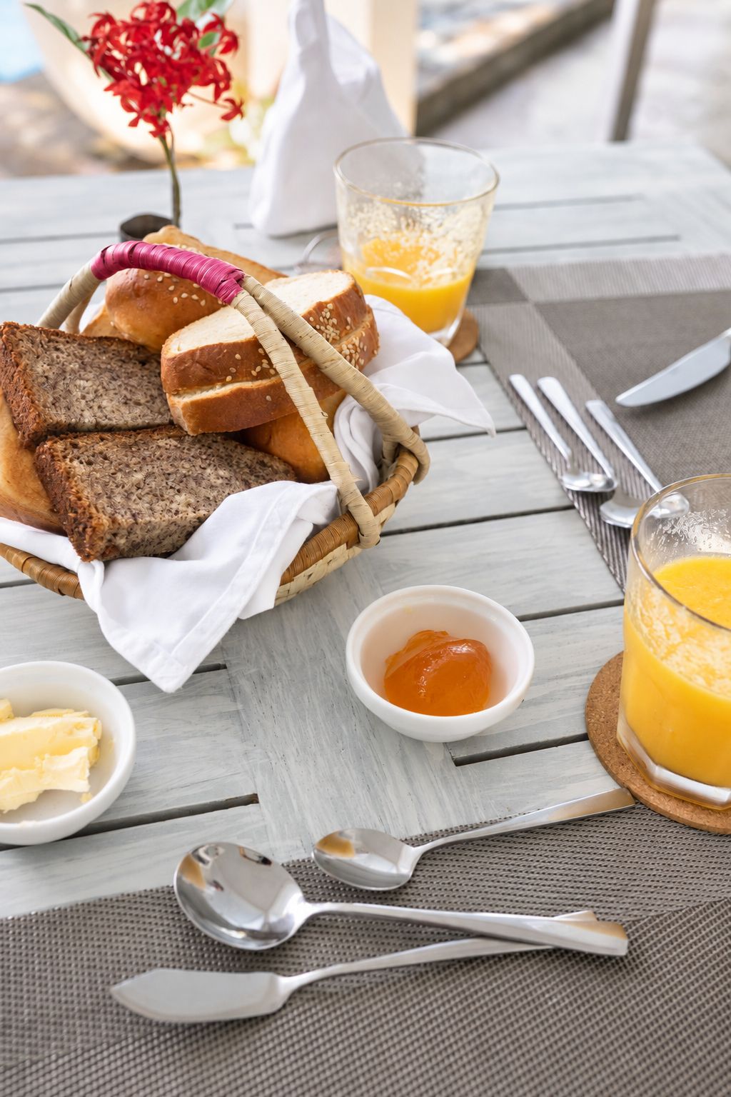A breakfast setting with bread, butter, jam, and orange juice on a wooden table.