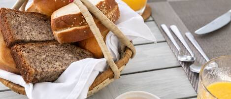 A breakfast setting with bread, butter, jam, and orange juice on a wooden table.