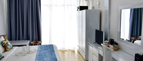 Ein Hotelzimmer mit Bett, Fernseher, Schreibtisch und einem großen Fenster mit Vorhängen.