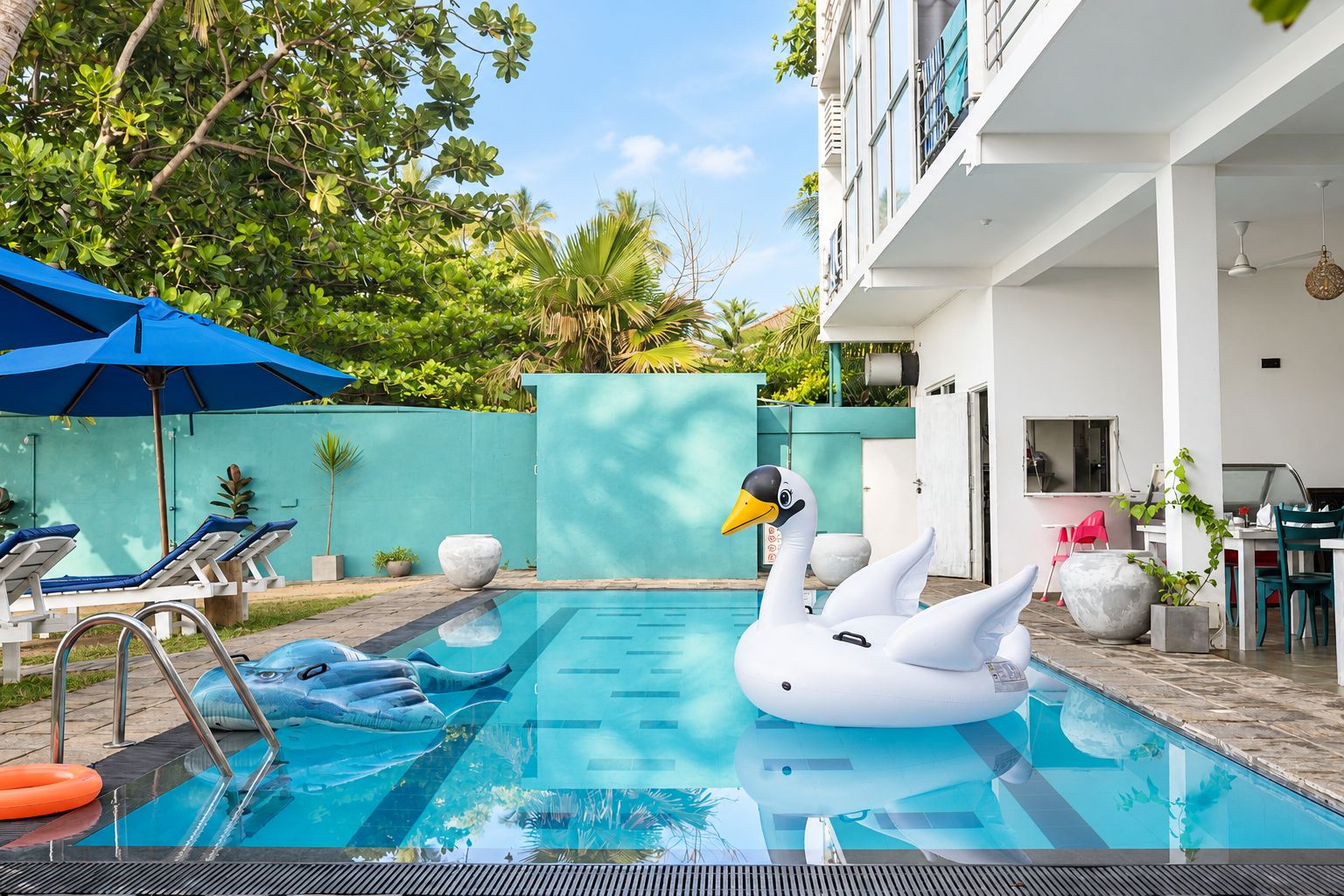 A swimming pool with two swan-shaped inflatable toys, lounge chairs, and a dining area with chairs and tables.