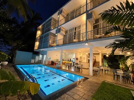 Um edifício de dois andares com piscina, área de estar externa e bar.