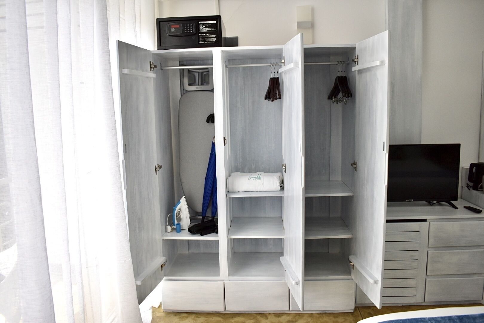 A walk-in closet with a microwave, ironing board, and hanging clothes.