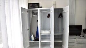 Ein begehbarer Kleiderschrank mit Mikrowelle, Bügelbrett und Kleiderstange.