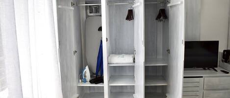 A walk-in closet with a microwave, ironing board, and hanging clothes.