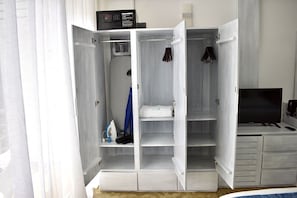 Ein begehbarer Kleiderschrank mit Mikrowelle, Bügelbrett und Kleiderstange.