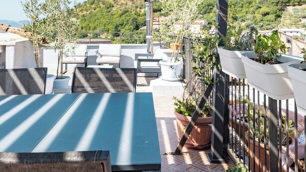 Una terrazza con tavolo e sedie, piante in vaso e vista su una collina.