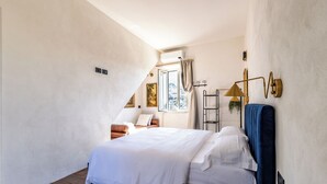 Una camera da letto con un letto grande, un tavolino, una sedia, una finestra con tende e una lampada a parete.