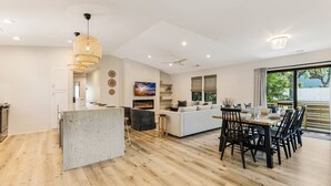 Une cuisine moderne dotée d’un îlot central, un coin repas avec une table et des chaises en bois, et un espace de vie avec un canapé et un téléviseur.
