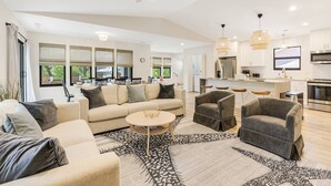 Un salon moderne comprenant un canapé, des fauteuils et une table basse. Il y a également un coin cuisine avec un réfrigérateur, une cuisinière et un espace repas.