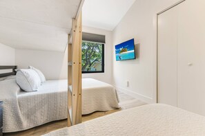 Een slaapkamer met twee bedden, een televisie aan de muur en een raam met uitzicht op bomen.