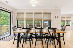 A dining area with a wooden table and black chairs, large windows with blinds, and a view of greenery outside. - Wonderful Dog Friendly Beach Home with Golf Cart (Oak Island)
