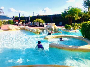 A swimming pool area with multiple water features, including a small waterfall and a circular water slide.