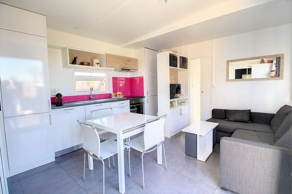 A modern kitchen with white cabinets, a pink backsplash, and a dining area with a white table and chairs.