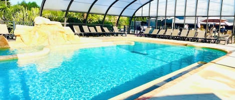 En pool med ett böjt glastak, solstolar och en klippformation.